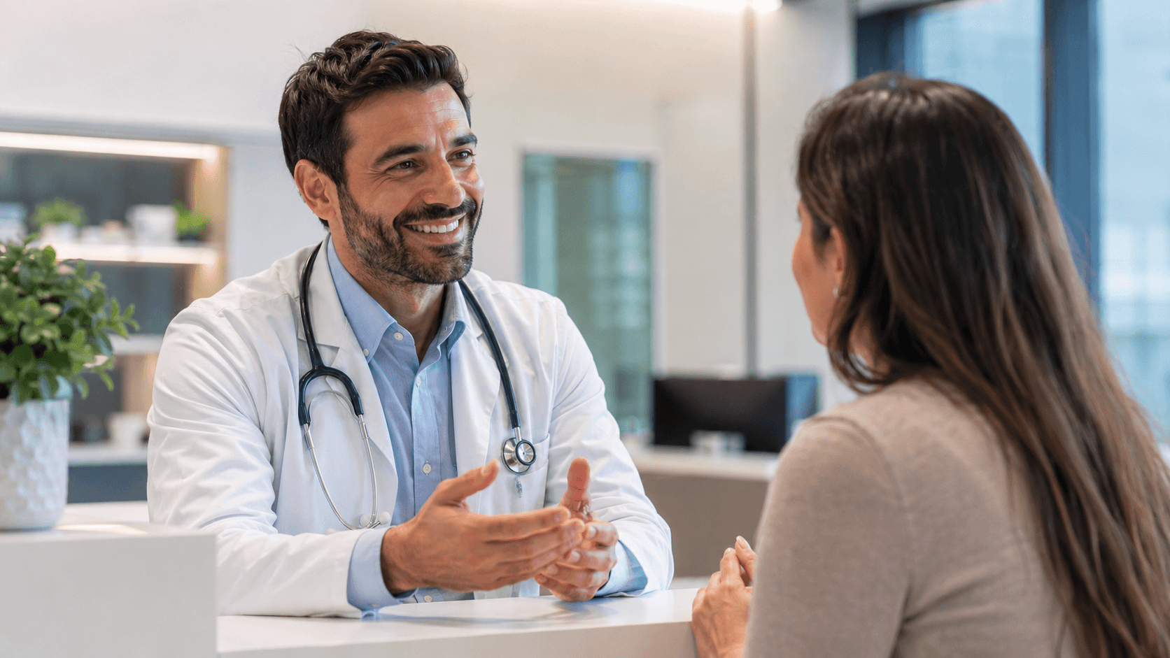 Healthcare professional speaking with a patient in a bright clinic reception area.